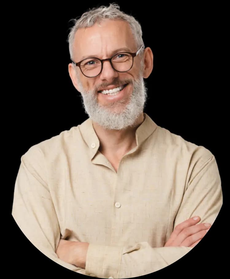 An elderly man with light skin and a full gray beard, wearing glasses and a beige shirt. He is smiling confidently with his arms crossed.